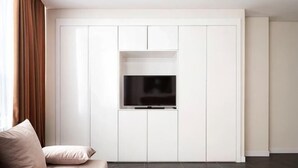 A living room with a sofa, a flat-screen TV mounted on a white cabinet, and a brown rug. - Highvill Hotel (Astana)
