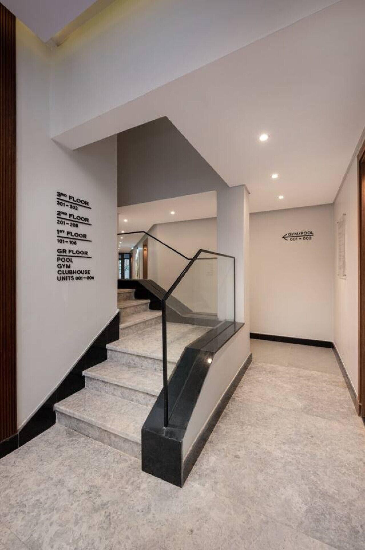 A modern staircase with glass railings and a marble floor, leading to a second-floor area with a sign indicating the location of the gym and pool.