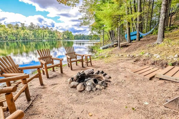 A lakeside setting with wooden chairs and a fire pit. - Spacious Pet-Friendly Lake Home with 2 Kitchens – Perfect for Family Gatherings (Lac du Flambeau)