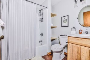 A bathroom with a shower curtain, a toilet, a sink with a mirror, and a framed picture on the wall. - Spacious Pet-Friendly Lake Home with 2 Kitchens – Perfect for Family Gatherings (Lac du Flambeau)