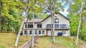 A two-story house with a covered porch and a staircase leading to the entrance. - Spacious Pet-Friendly Lake Home with 2 Kitchens – Perfect for Family Gatherings (Lac du Flambeau)