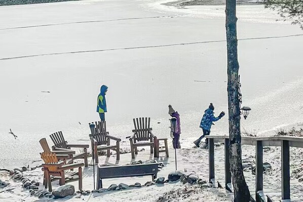Une plage avec des chaises en bois et un banc, un arbre, et une personne qui se promène.