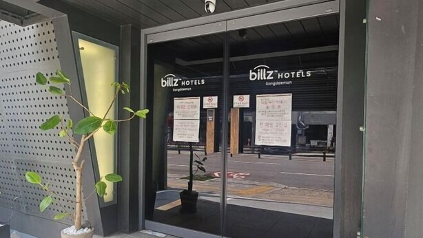 Der Eingang des Billz Hotels mit modernem Design, darunter Glastüren und ein Blumentopf.