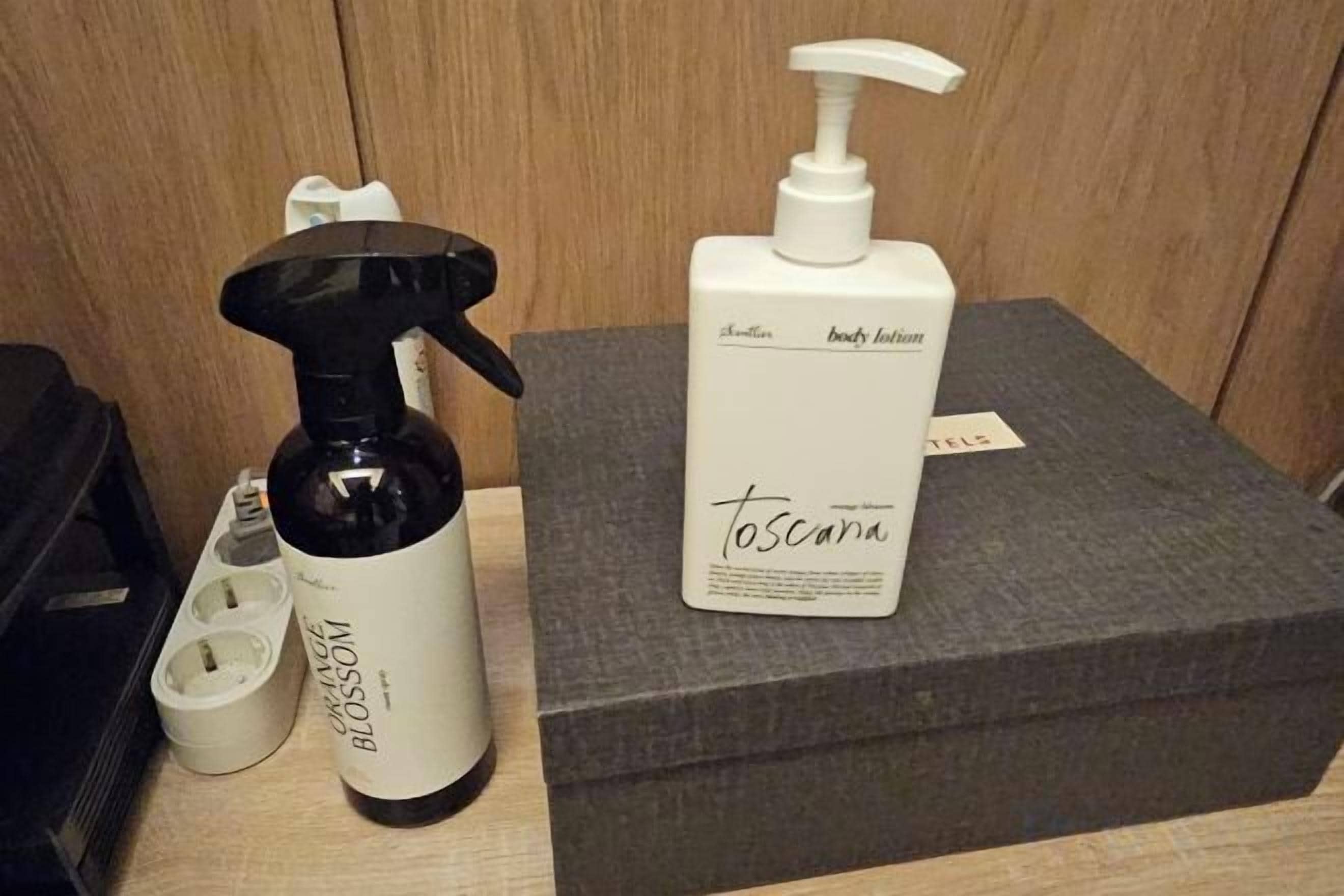 A bathroom with a black bottle of body lotion, a white bottle of body lotion, and a white box with the brand name 'toscana' on it.