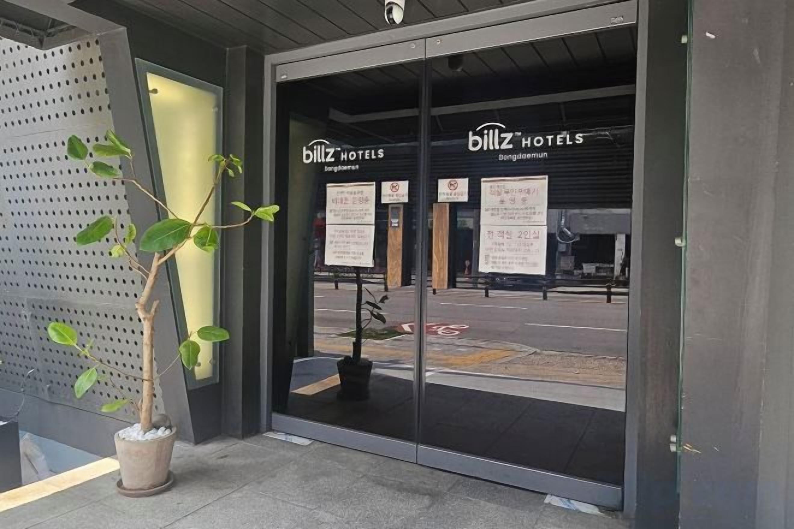 The entrance to a hotel with glass doors, a potted plant, and informational signs.