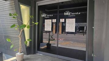 The entrance to a hotel with glass doors, a potted plant, and informational signs.