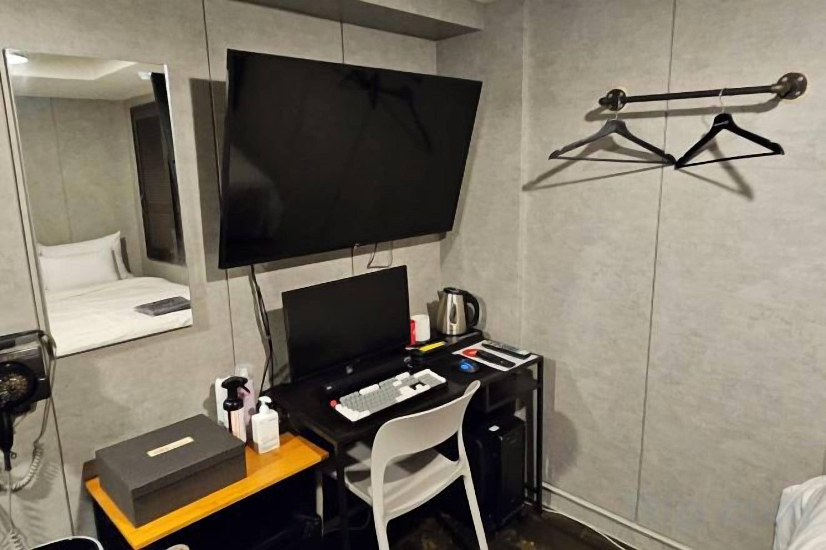 A hotel room with a bed, a desk with a computer, a chair, a TV, and a coat rack.