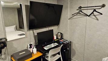 A hotel room with a bed, a desk with a computer, a chair, a TV, and a coat rack.
