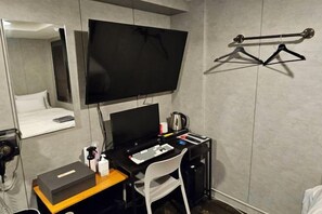 Een hotelkamer met een bed, een bureau met een computer, een stoel, een televisie en een kapstok.