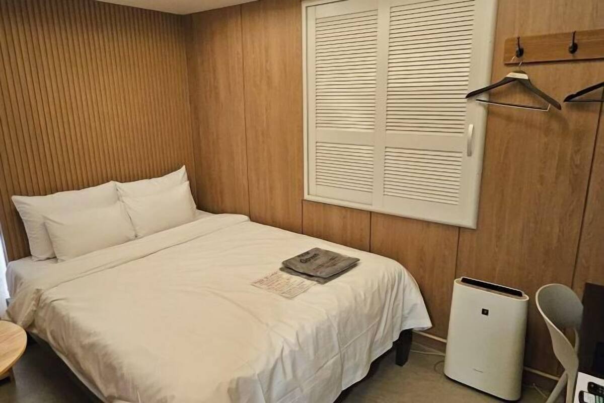 Ein Schlafzimmer mit einem Bett, einem Fenster mit Jalousien, einem Heizkörper und einem Sessel.