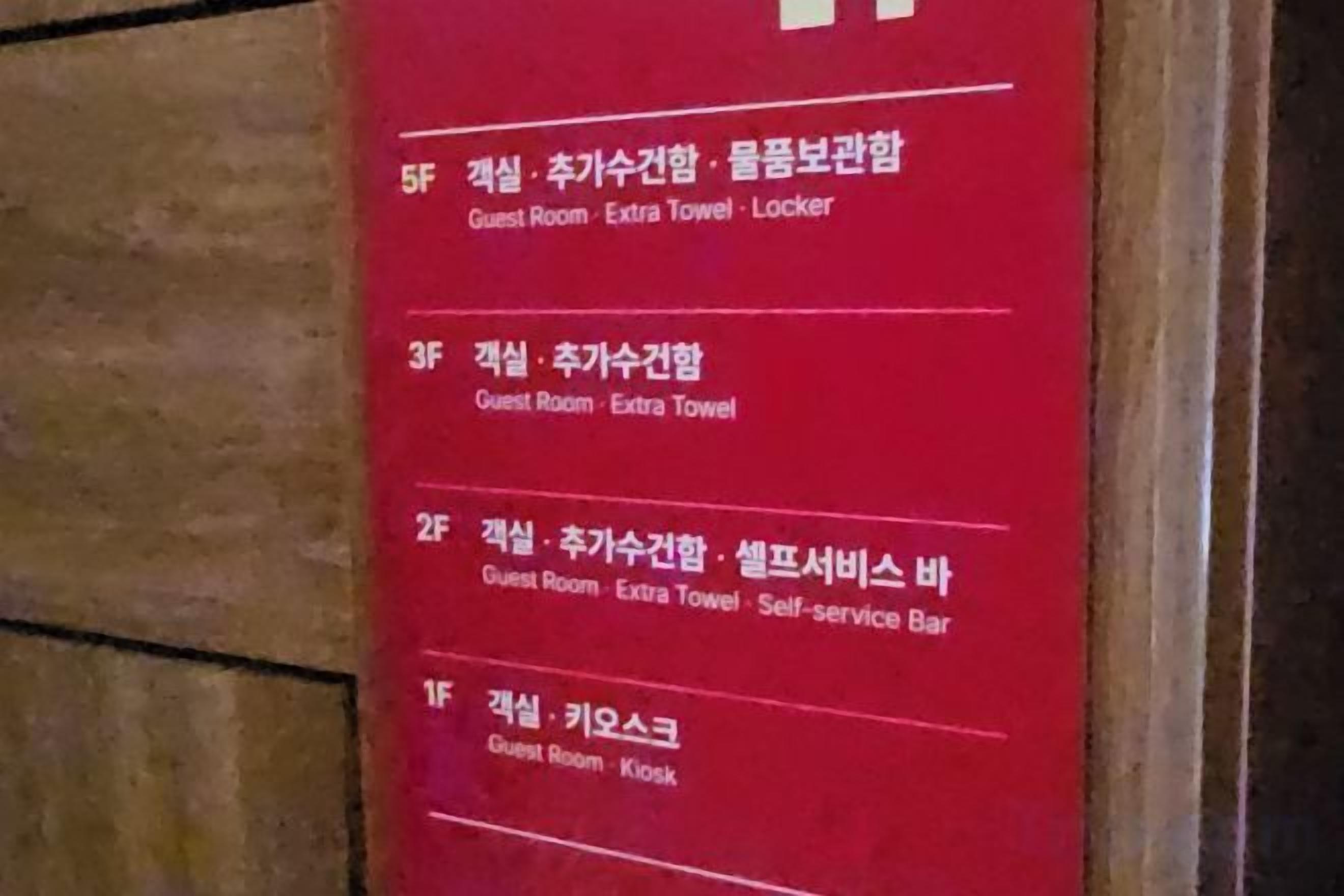A red sign with room numbers and descriptions in Korean, including a guest room with a locker.