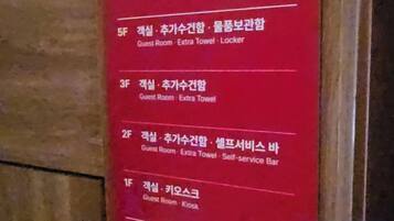 A red sign with room numbers and descriptions in Korean, including a guest room with a locker.
