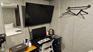 Ein Hotelzimmer mit einem Bett, einem Schreibtisch mit Computer, einem Fernseher und einem Kleiderhaken.