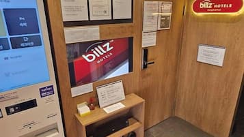 A hotel reception area with a digital kiosk, a reception desk, and various informational signs.