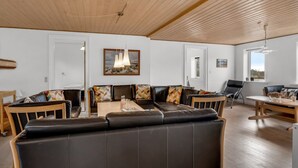 Ein modernes Wohnzimmer mit Holzboden, einem schwarzen Ledersofa, einem Holzesstisch und Blick ins Freie durch ein Fenster.
