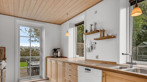Eine moderne Küche mit Holzausstattung, einem Geschirrspüler und einem großen Fenster mit Blick ins Freie.