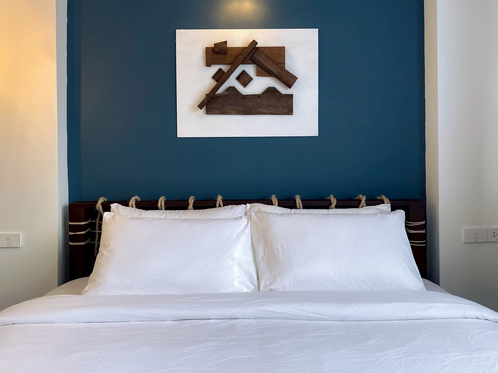 A bed with white linens and a wooden headboard against a blue wall.
