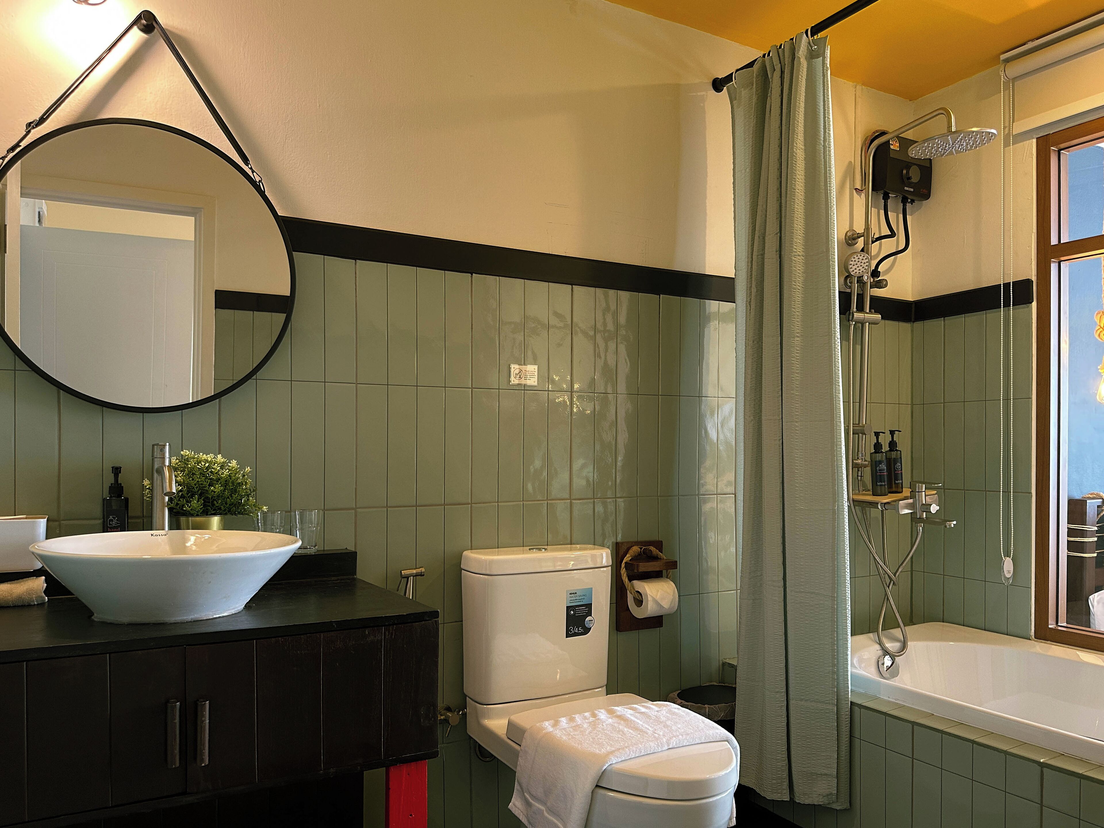 A bathroom with a toilet, sink, mirror, shower, and a window.