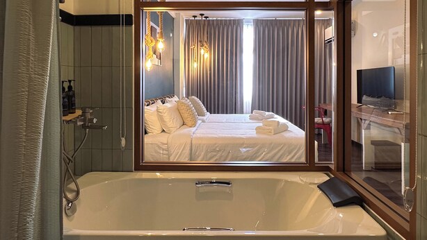 A modern hotel room with a large bathtub, a bed with white linens, and a desk with a computer. - belivin'98 Sense of Pier Sathorn (Bangkok)