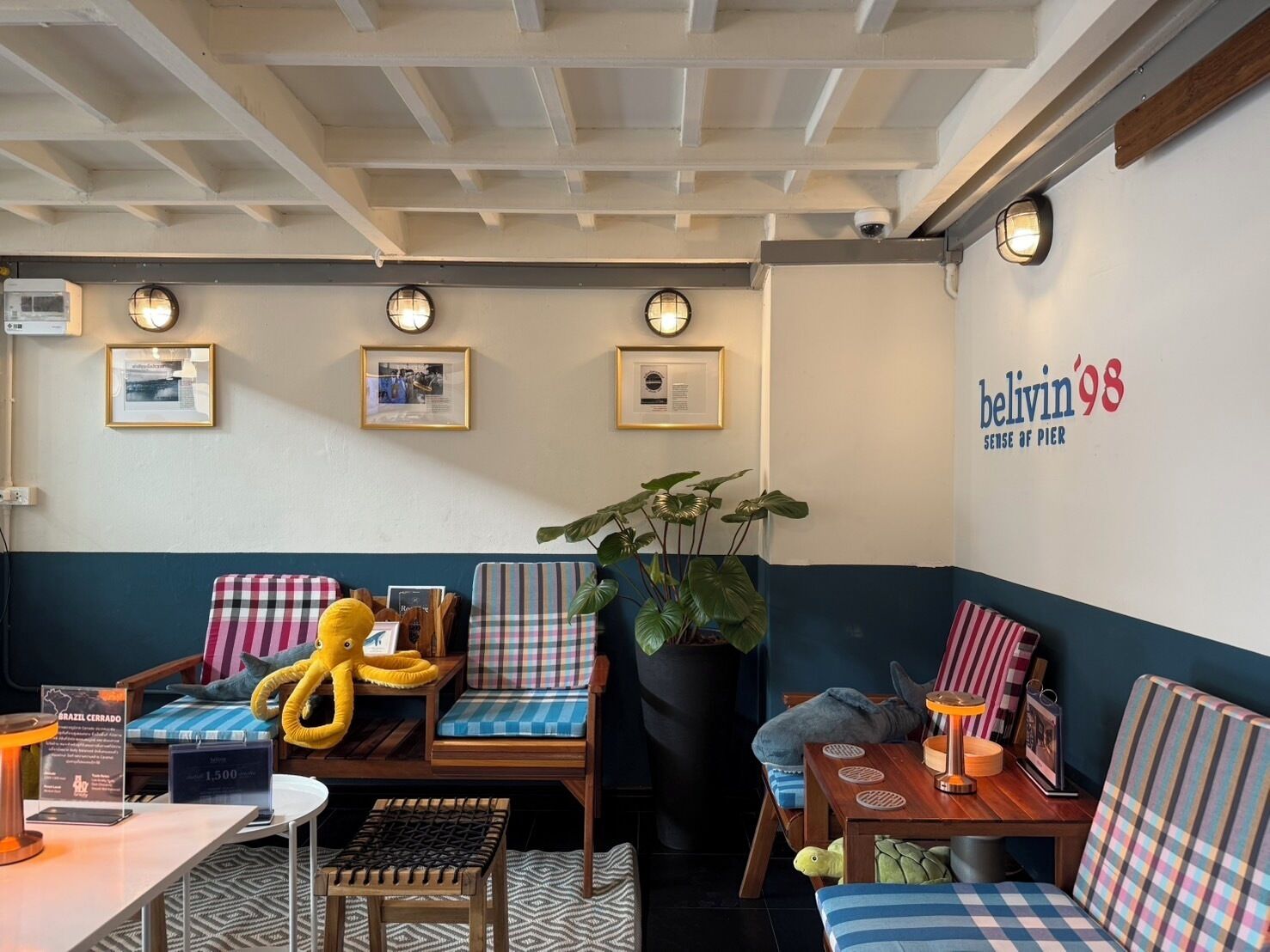 Un espace salon accueillant, avec des sièges, une grande plante en pot et un mur orné d’une enseigne.