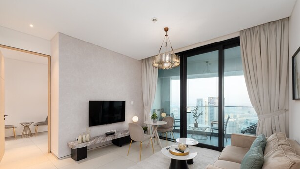 A modern living room with a sofa, coffee table, TV, and a balcony with a city view. - Modern 1BR w/ Marina View Balcony at Address JBR (Dubai)