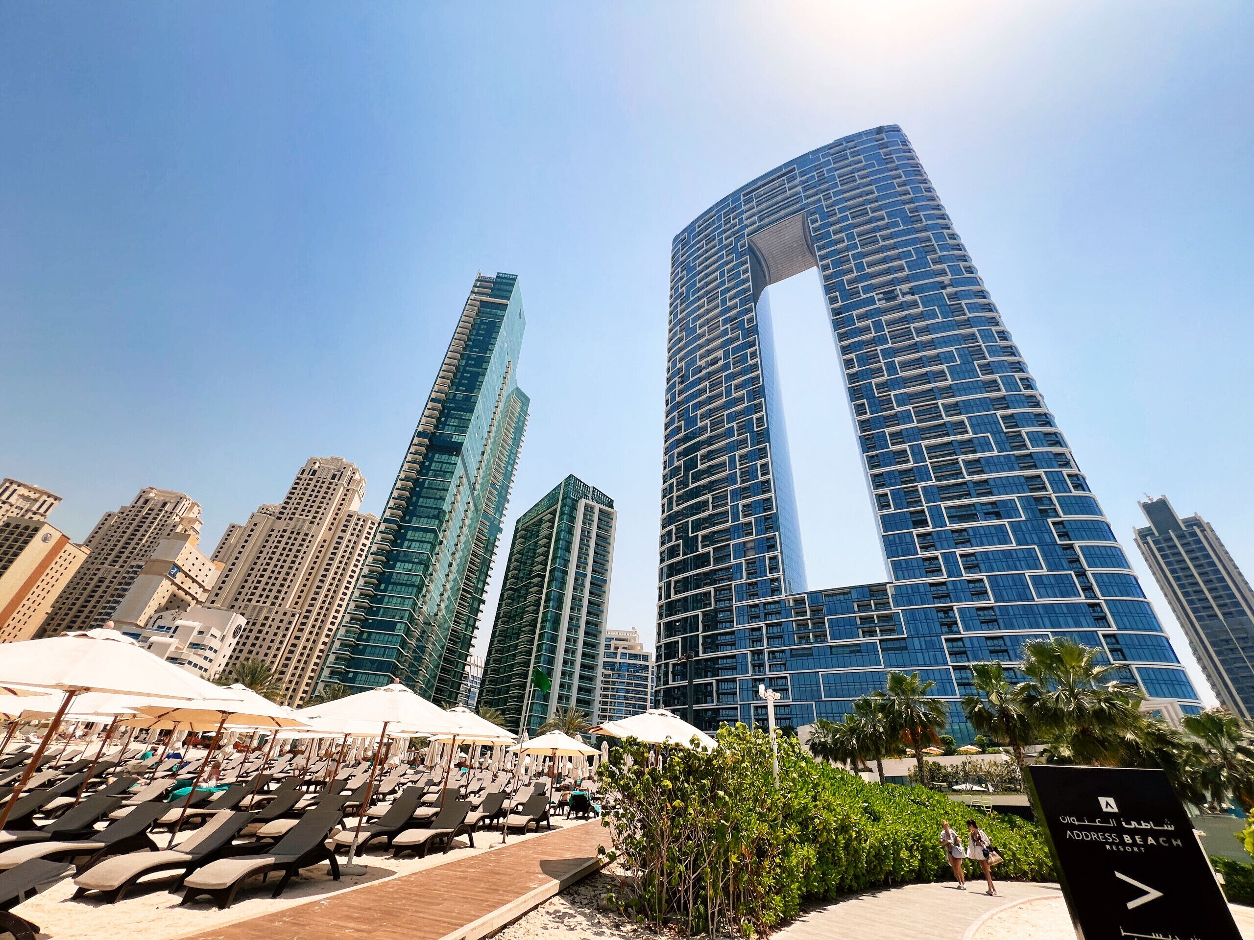 A modern resort with a beach area, including sun loungers and umbrellas, and a sign indicating the name of the resort.