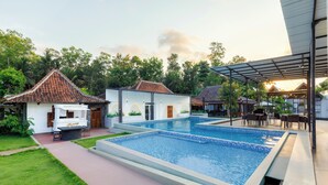 Una piscina con borde de baldosas, un puesto de comida y una zona de estar cubierta con mesas y sillas.