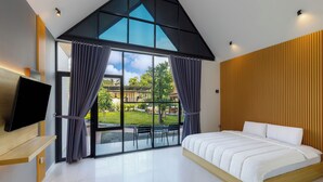 Un dormitorio moderno con una cama grande, un televisor sobre un soporte de madera y vistas a un jardín a través de amplios ventanales.