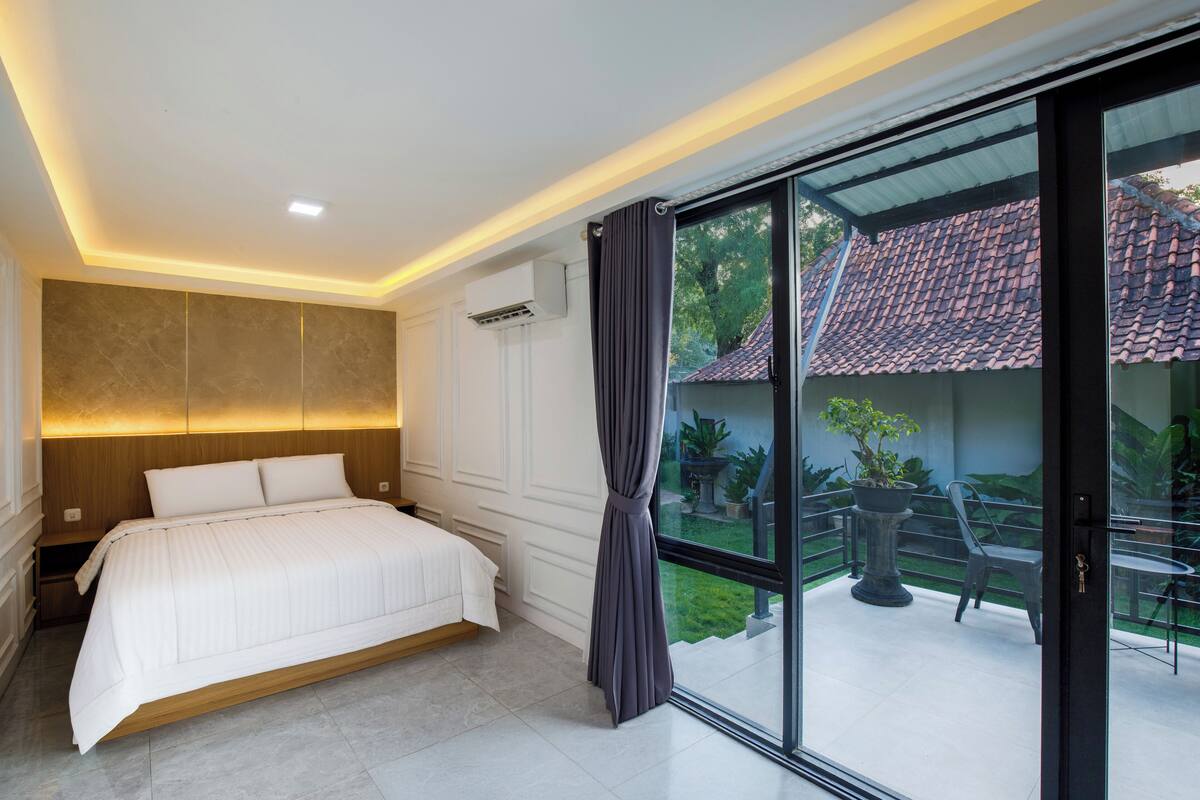Une chambre à coucher moderne avec un grand lit, une porte-fenêtre coulissante donnant sur un balcon et un plafond doté d’un éclairage encastré.