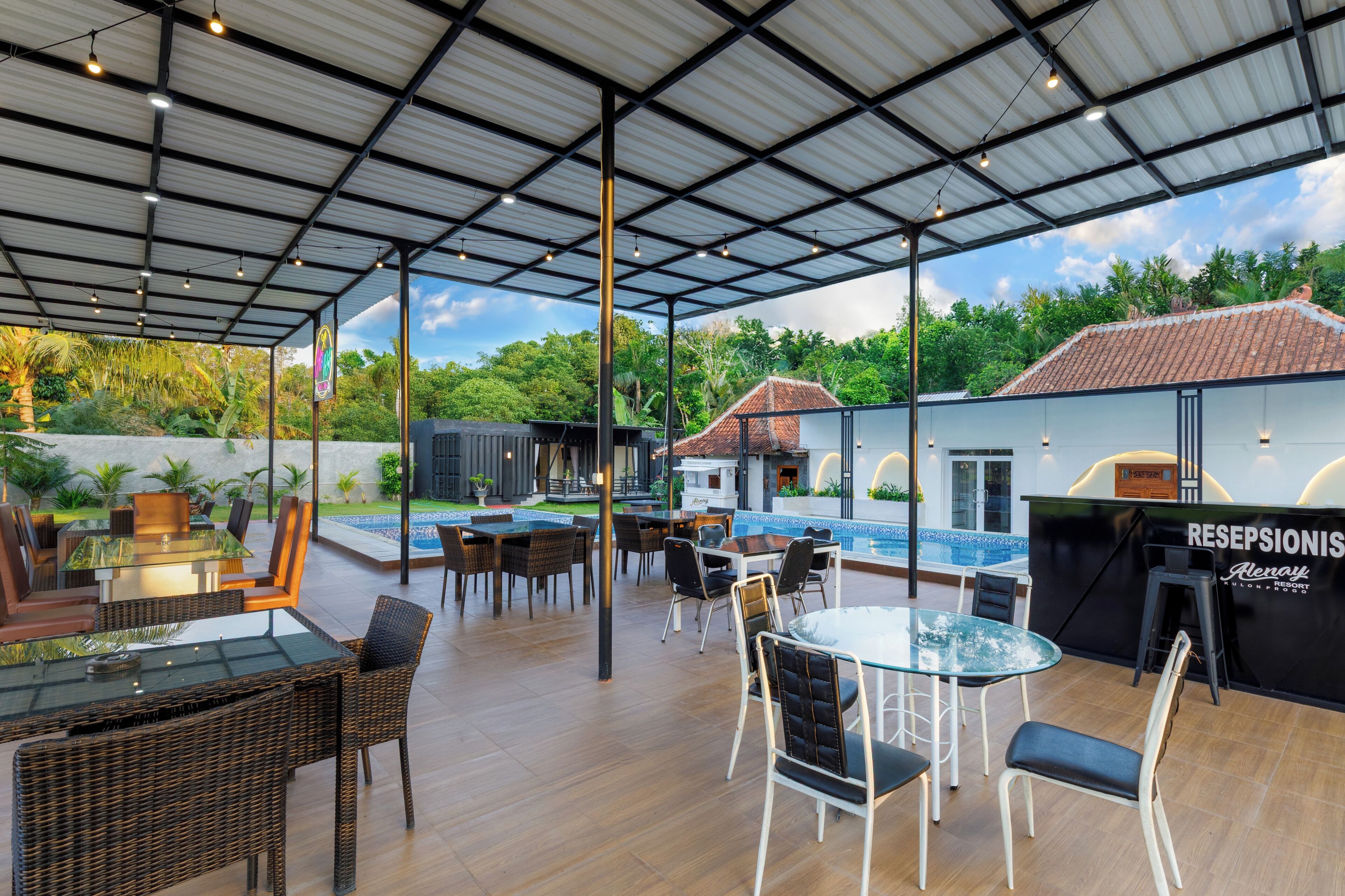 An outdoor patio area with tables and chairs, a reception desk, and a pool in the background.