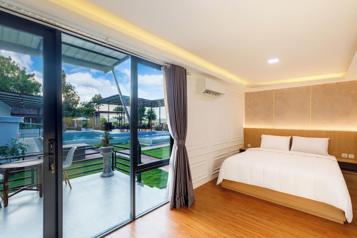 Une chambre d’hôtel moderne dotée d’un grand lit, d’une porte vitrée donnant sur un espace piscine et offrant une vue sur l’extérieur.