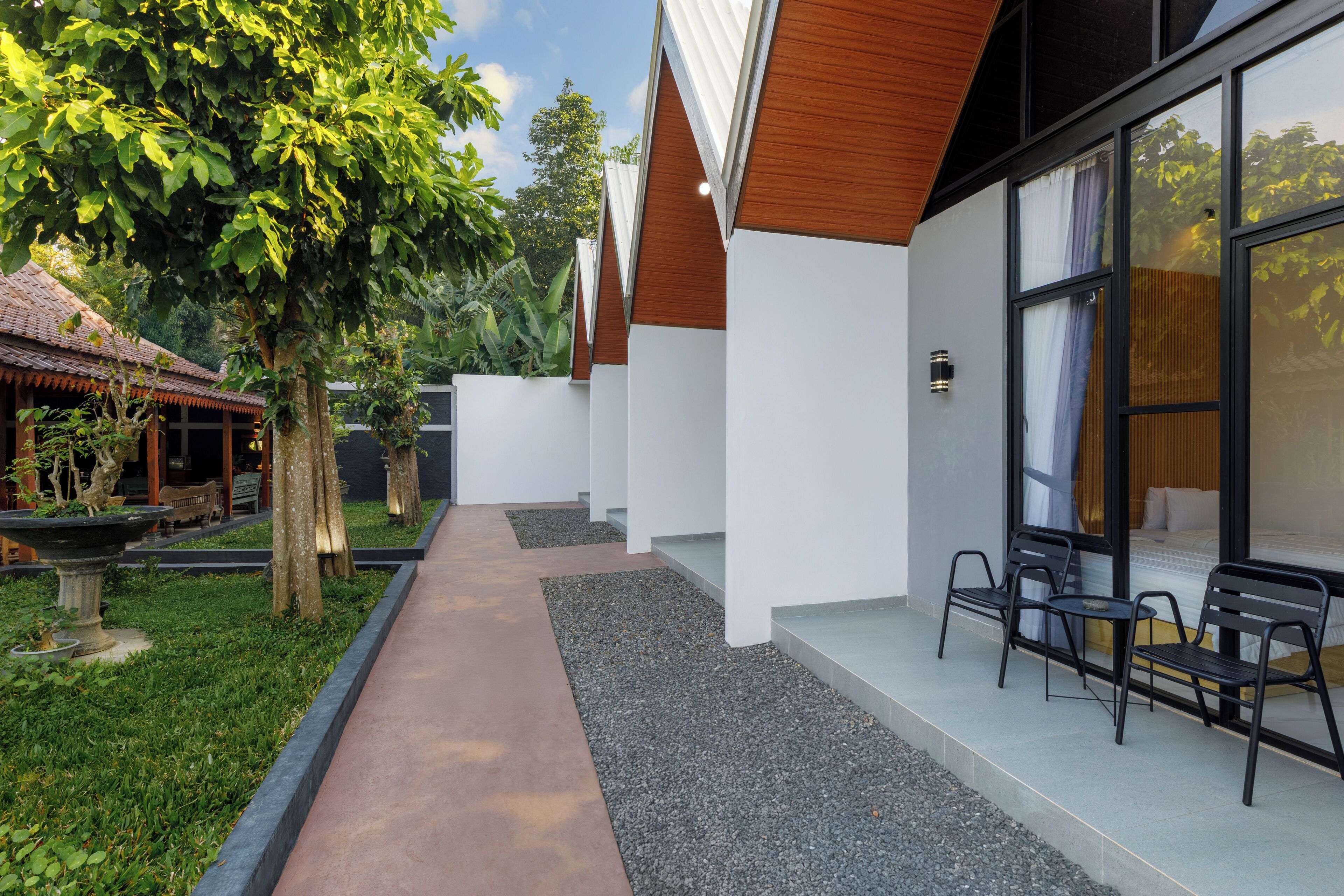 A modern building with a covered outdoor seating area, a pathway, and a garden with trees and plants.