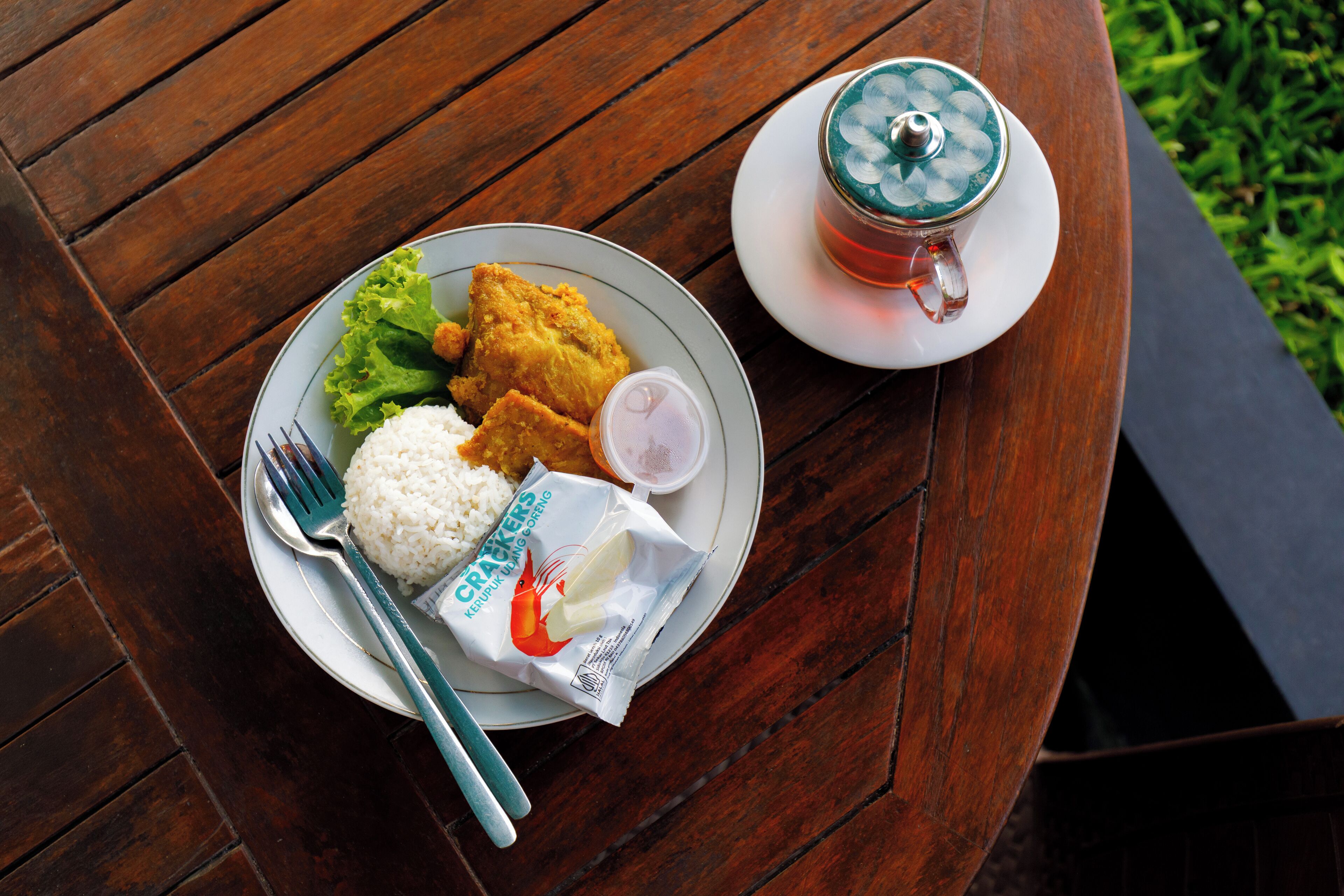 A wooden table with a plate of food including rice, fried items, and a packet of crackers.