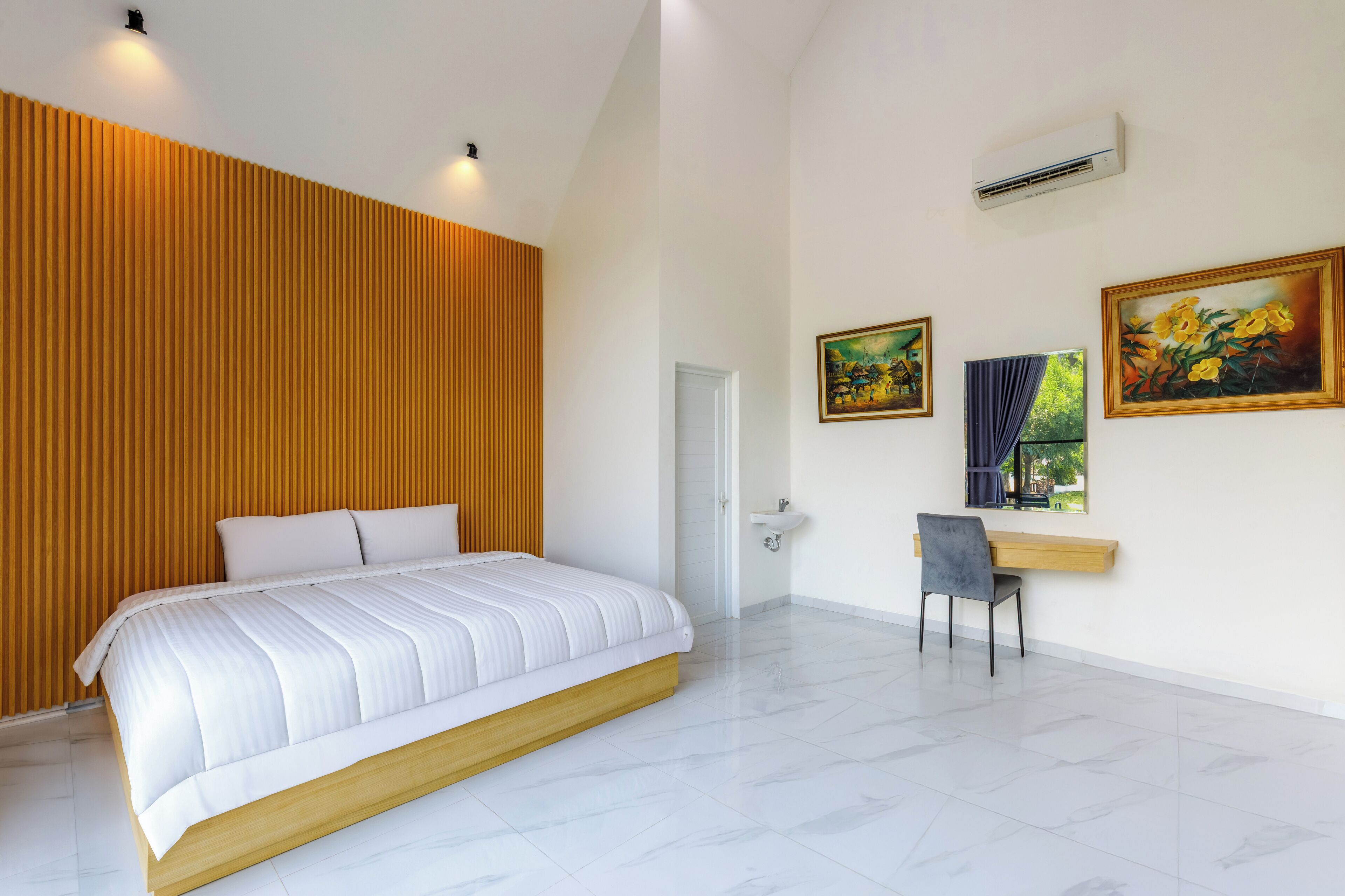 A bedroom with a large bed, a desk with a chair, and two paintings on the wall.