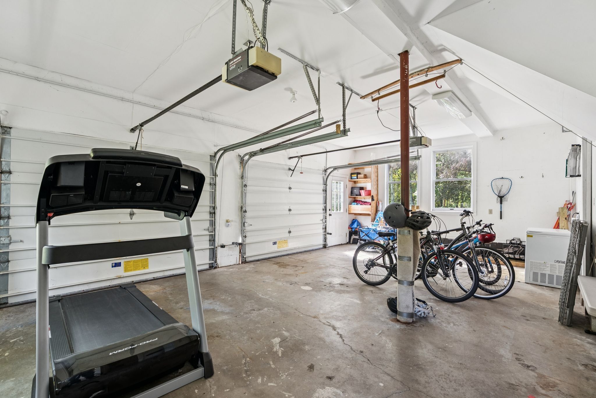 A garage with a treadmill, bicycles, and a ceiling fan.