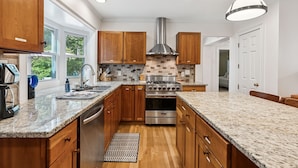 A kitchen with wooden cabinets, a stainless steel range hood, granite countertops, and a large window providing natural light. - 6 bedrooms! Hot tub/firepit/deck/Pet friendly close to beach! (Kennebunk)