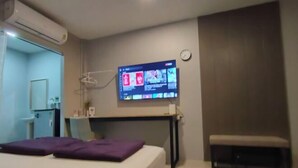 A bedroom with a bed, a TV mounted on the wall, a bench, and a small table. - Bunk Ubon Hostel (Ubon Ratchathani)