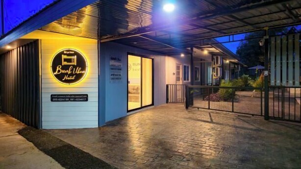 A hotel entrance with a neon sign, a paved walkway, and a covered area with a railing. - Bunk Ubon Hostel (Ubon Ratchathani)
