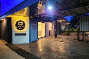 A hotel entrance with a circular sign, a covered walkway, and a gated driveway. - Bunk Ubon Hostel (Ubon Ratchathani)
