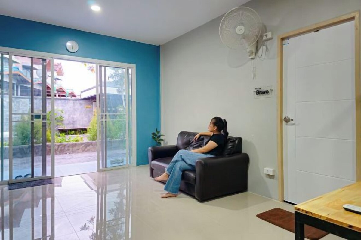 A room with a black leather sofa, a wooden table, a white door, and a fan on the wall.