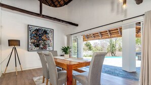 Un comedor con una mesa de madera y sillas grises, una planta en maceta y un cuadro abstracto grande en la pared.