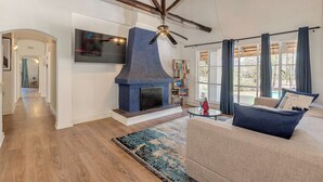 Una sala de estar con chimenea de piedra, vigas de madera, ventilador de techo, sofá, mesa de centro y estantería.