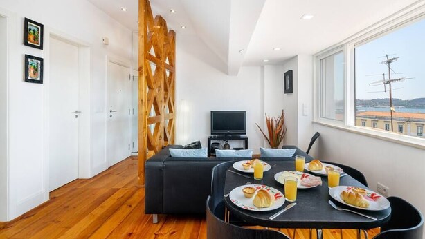 Quarto moderno com uma mesa de jantar posta para o café da manhã, um sofá, uma televisão e vista para a cidade.