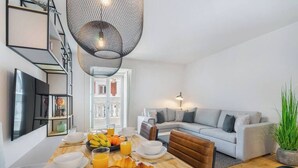Ein modernes Wohnzimmer mit Essbereich, ausgestattet mit einem Holztisch, der für das Frühstück gedeckt ist, einem grauen Sofa und einer Pendelleuchte.