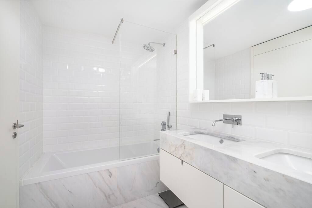 Een moderne badkamer met een douchecabine van glas, een wit marmeren wastafel en een grote spiegel.