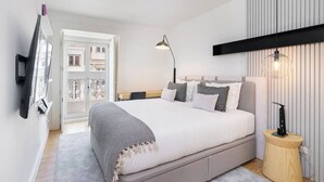 Ein modernes Schlafzimmer mit einem großen Bett, einem Nachttisch mit Lampe und Blick durch eine Glastür nach draußen.