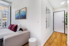 A modern room with a bed, a small sofa, and a window with a view of buildings. - Alcântara Smart Studio | AC | Lx Factory (Lisboa)