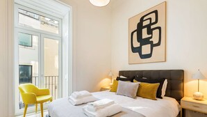 A hotel room with a bed, a chair, a bedside table, a lamp, and a large abstract painting on the wall. - Liberdade Deluxe Apartment | AC | S-Pool | Parking (Lisboa)