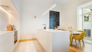 A modern kitchen with white cabinetry, a central island, and a dining area with yellow chairs. - Liberdade Deluxe Apartment | AC | S-Pool | Parking (Lisboa)
