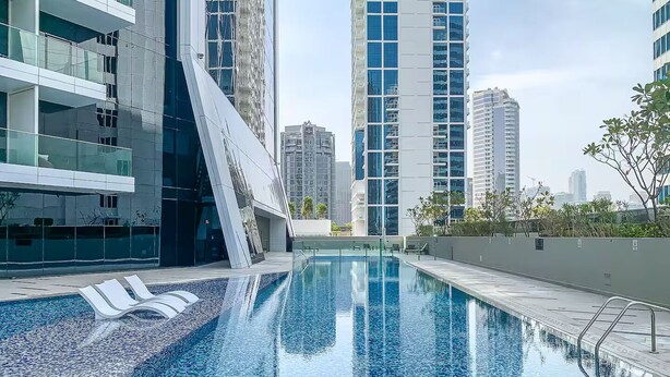 A modern building with a pool area, featuring a clear pool, lounge chairs, and high-rise buildings in the background. - Marquise Square Towers - Business Bay (Dubai)